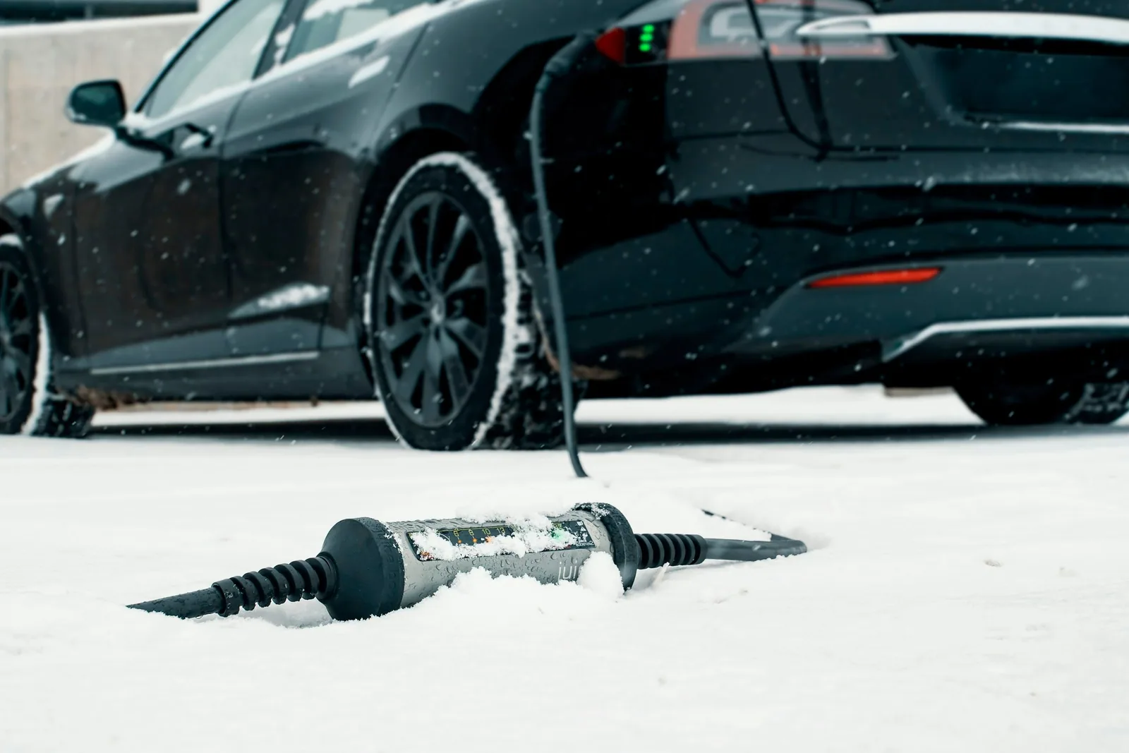 Voiture électrique noire en charge dans la neige, le câble posé sur le sol enneigé