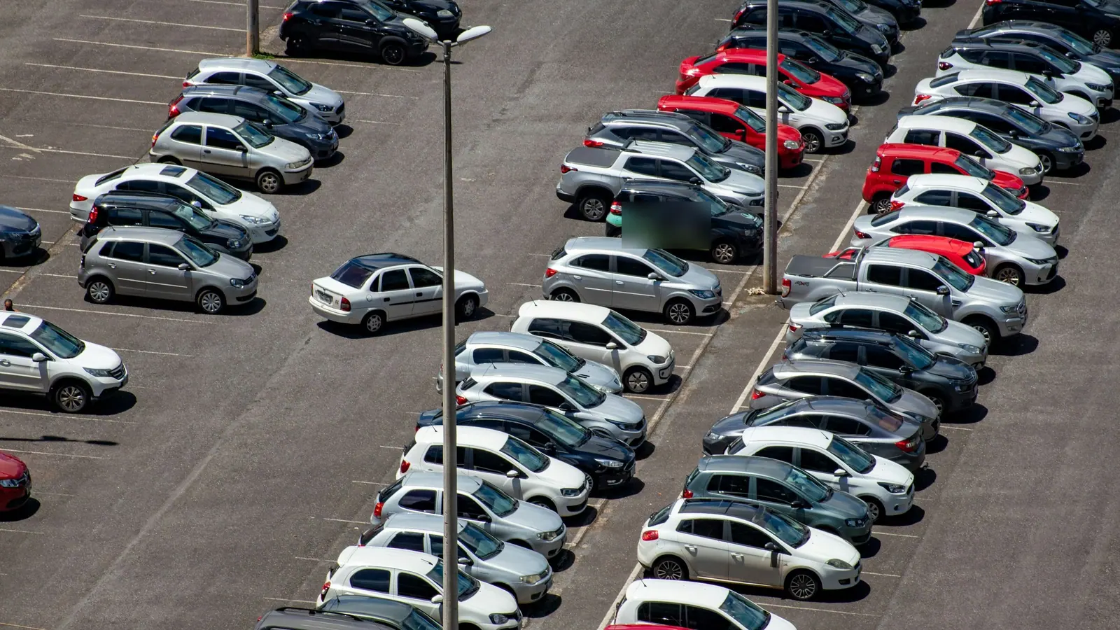 Grand parking vu d’en haut, dominé par des voitures blanches, grises et noires, avec quelques rouges