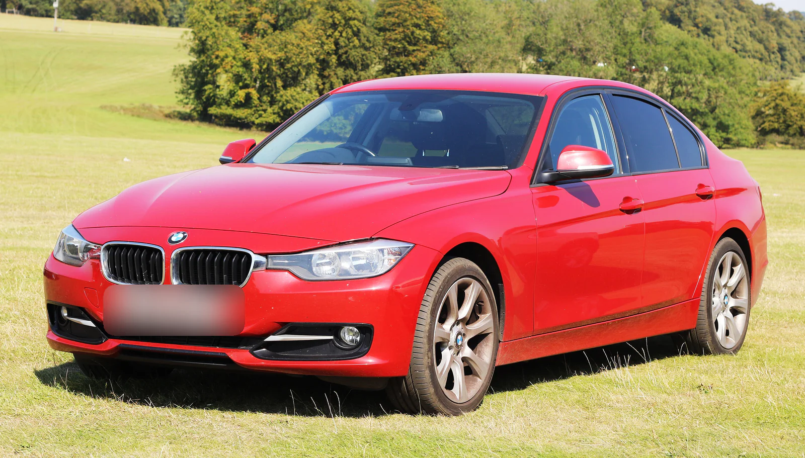 BMW 320d berline F30 rouge de 2012 garée sur l’herbe, vue de trois quarts avant