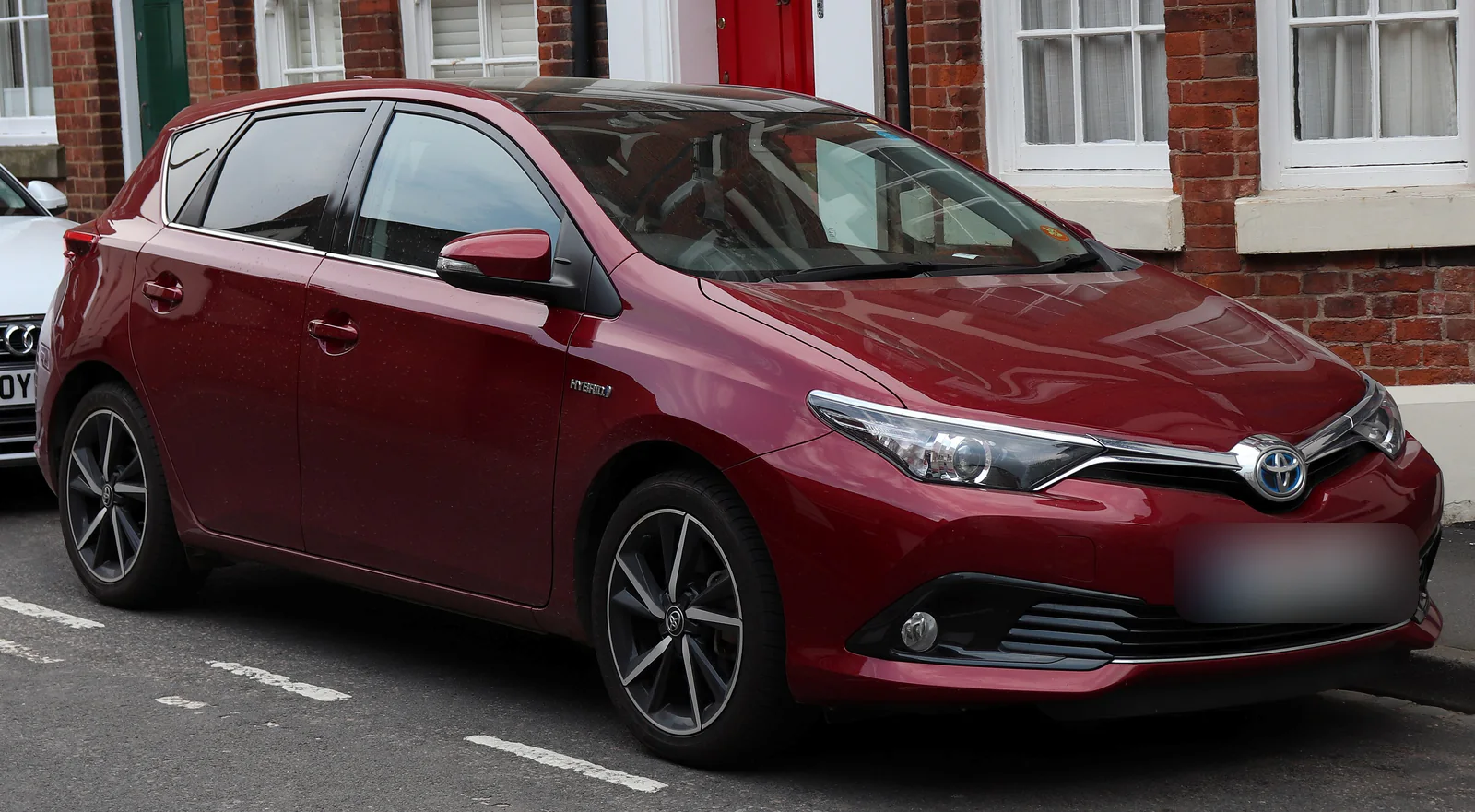 Toyota Auris hybride de deuxième génération rouge garée dans une rue, vue de trois quarts avant