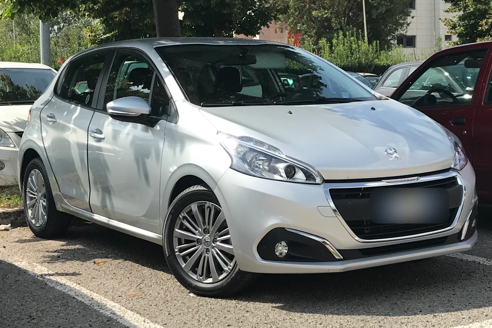 Peugeot 208 de première génération grise, cinq portes, garée sur un parking, vue de trois quarts avant