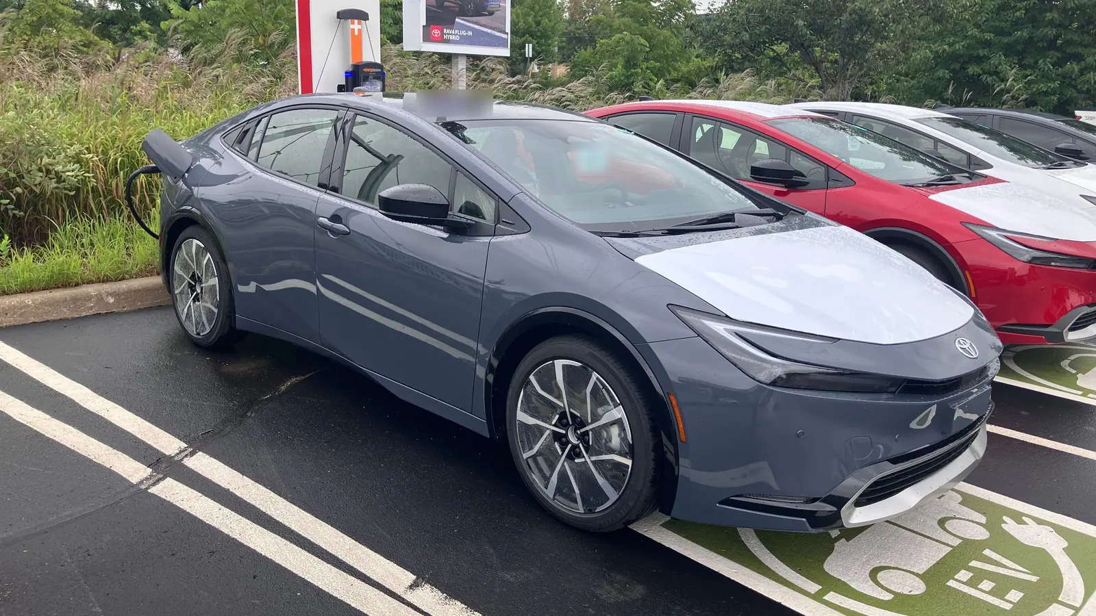 Toyota Prius hybride rechargeable grise garée sur une place de recharge, devant une borne
