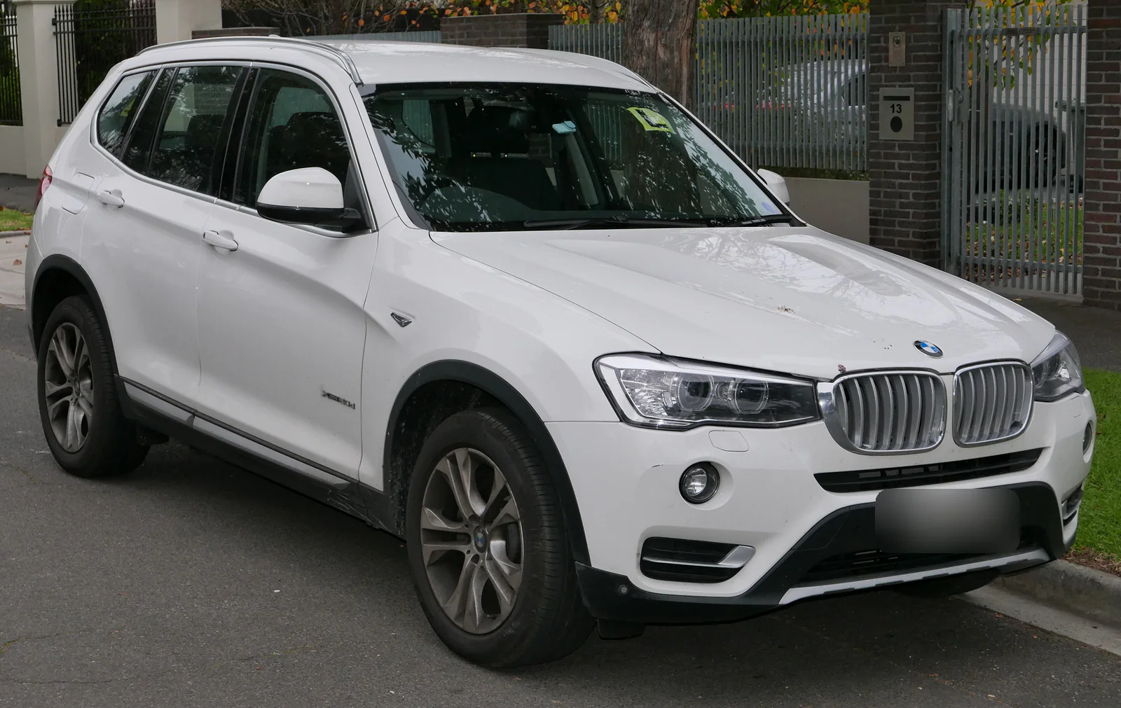BMW X3 F25 restylé blanc garé devant une maison, vue de trois quarts avant