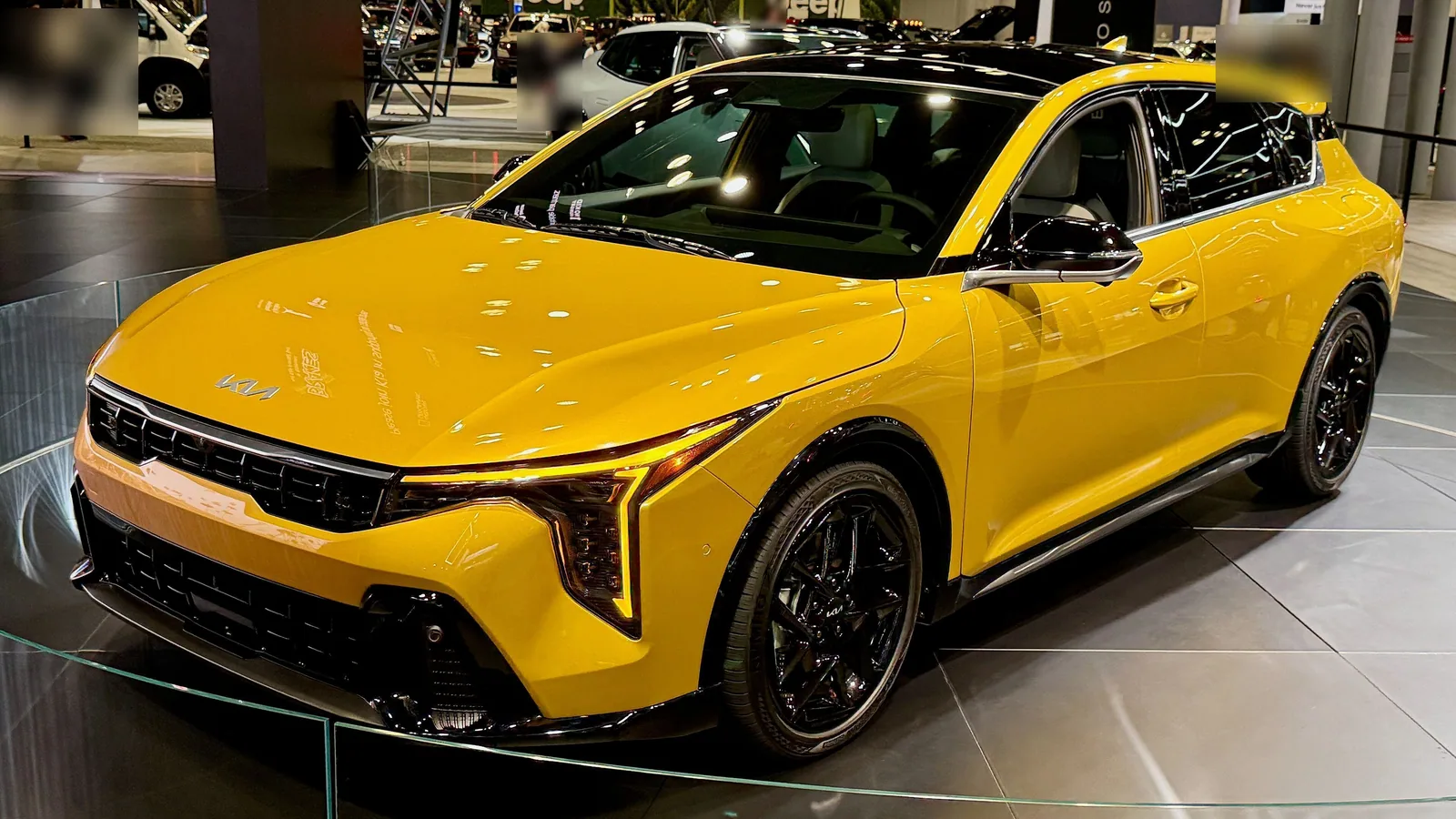 Kia K4 cinq portes jaune exposée dans un salon automobile, vue de trois quarts avant