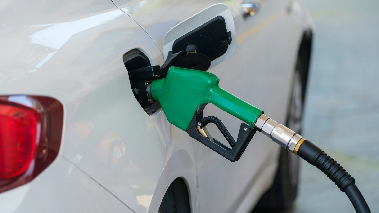 Pistolet vert de carburant sans plomb engagé dans le réservoir d’une voiture blanche