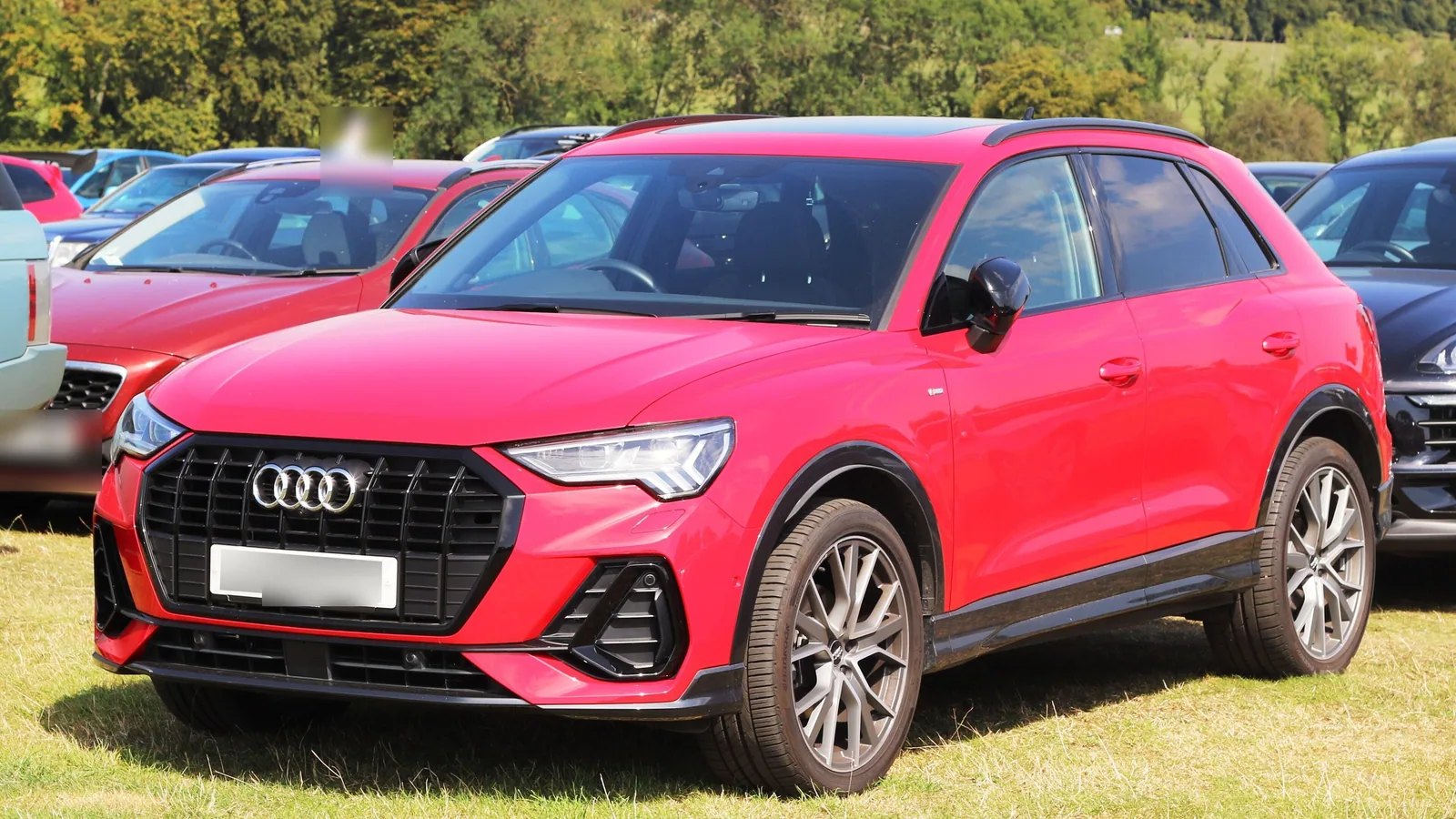 Audi Q3 rouge de deuxième génération garée sur l’herbe parmi d’autres Audi