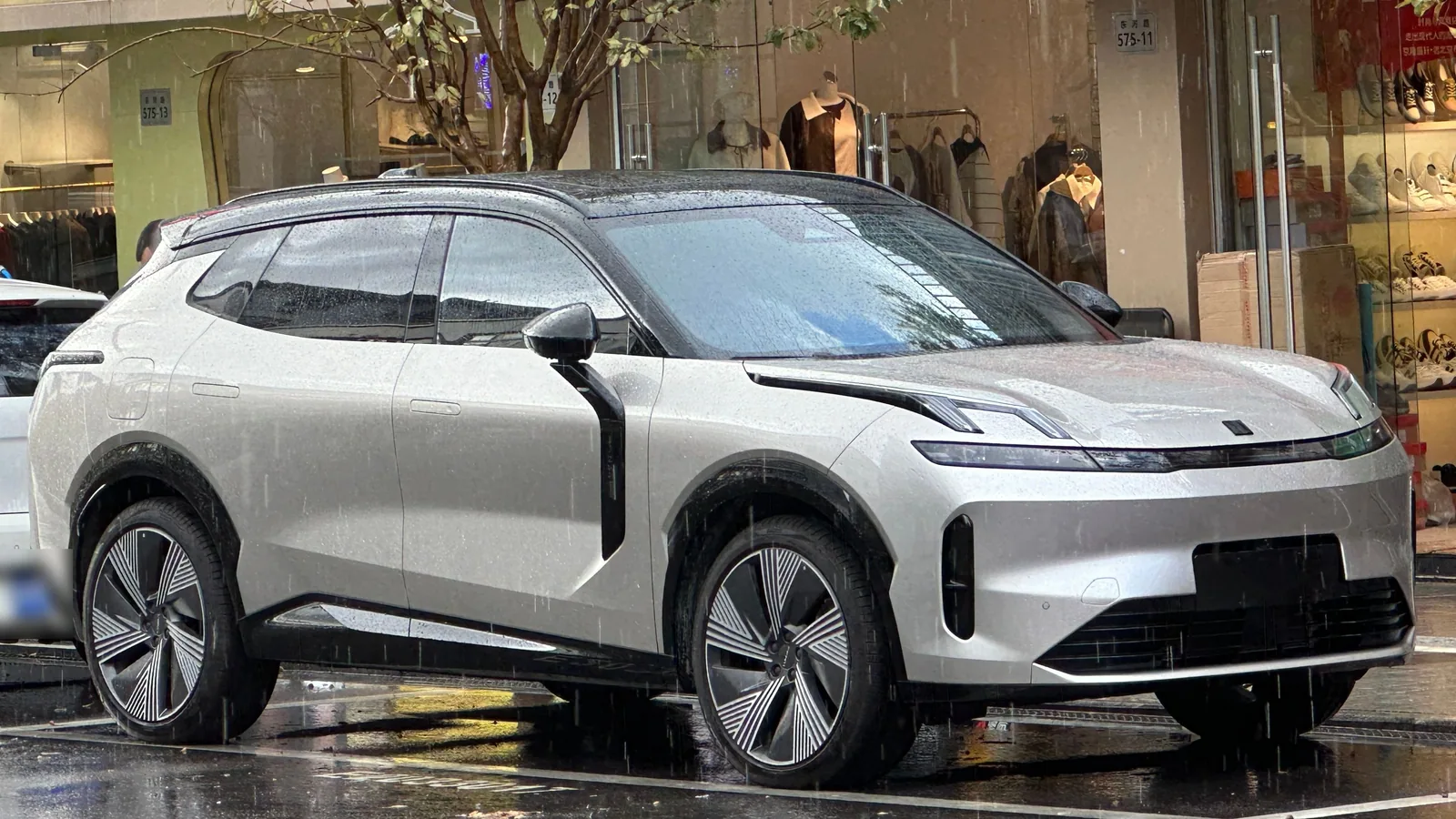 Lynk & Co 08 gris clair garé devant une vitrine, vue de trois quarts avant