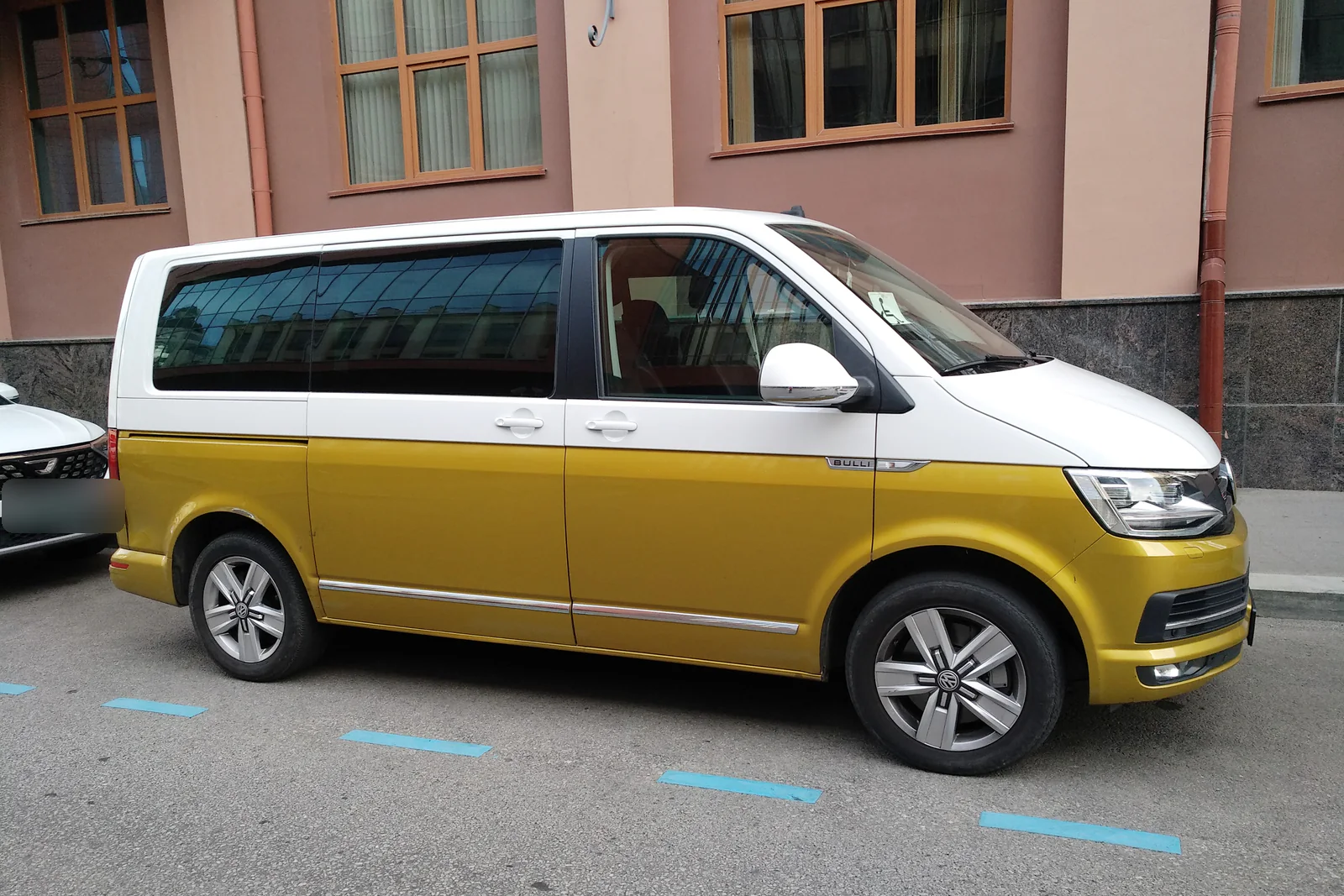 Volkswagen Multivan T6 bicolore blanc et doré garé le long d’un trottoir, vue de trois quarts avant