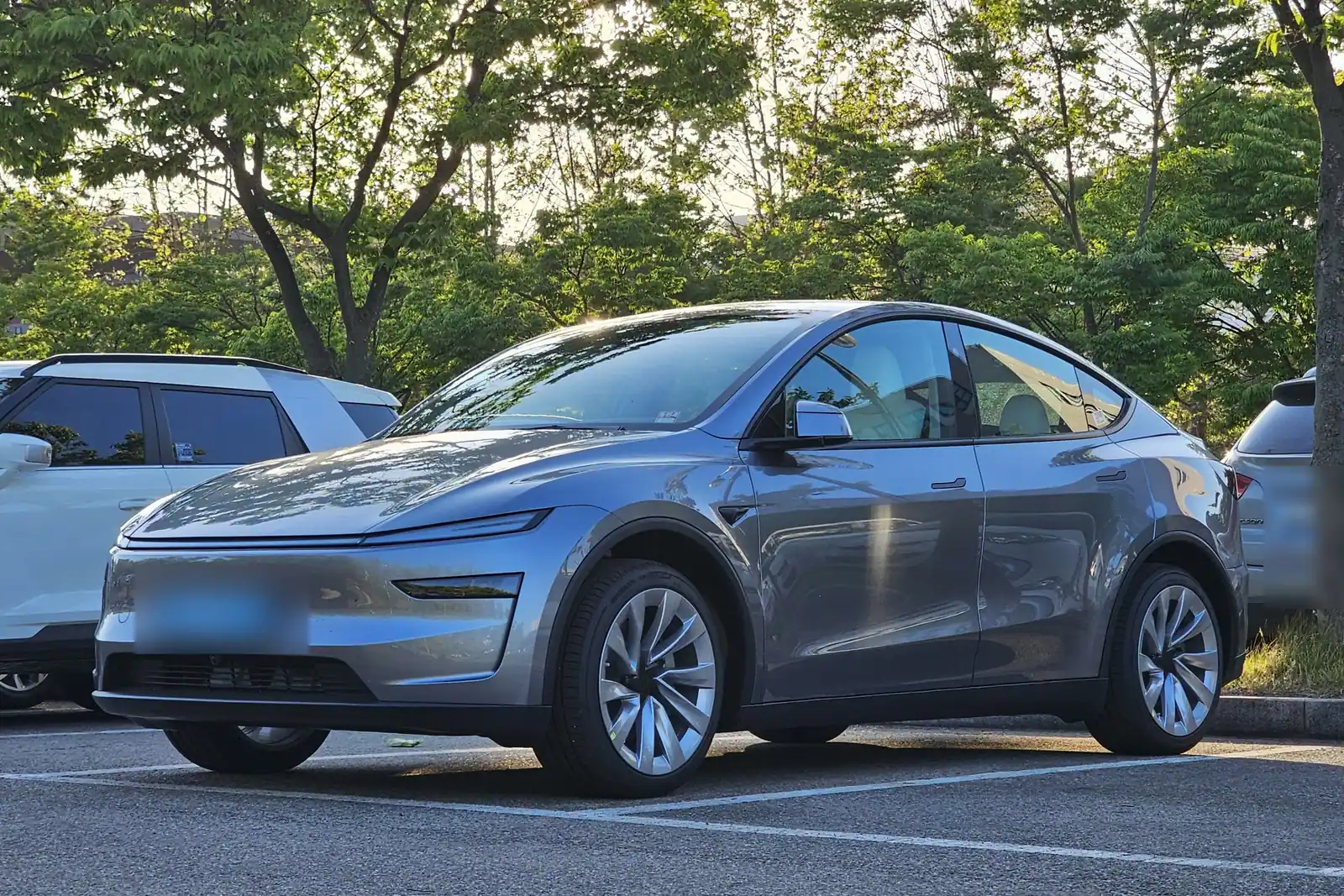 Tesla Model Y restylée gris argent garée sur un parking arboré