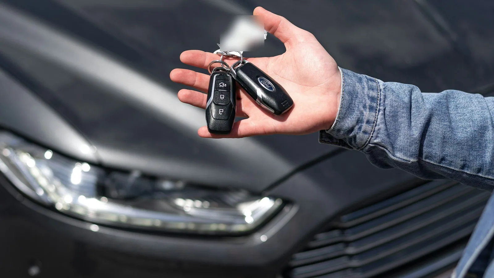 Main tendant une clé de voiture devant le capot d’une berline sombre