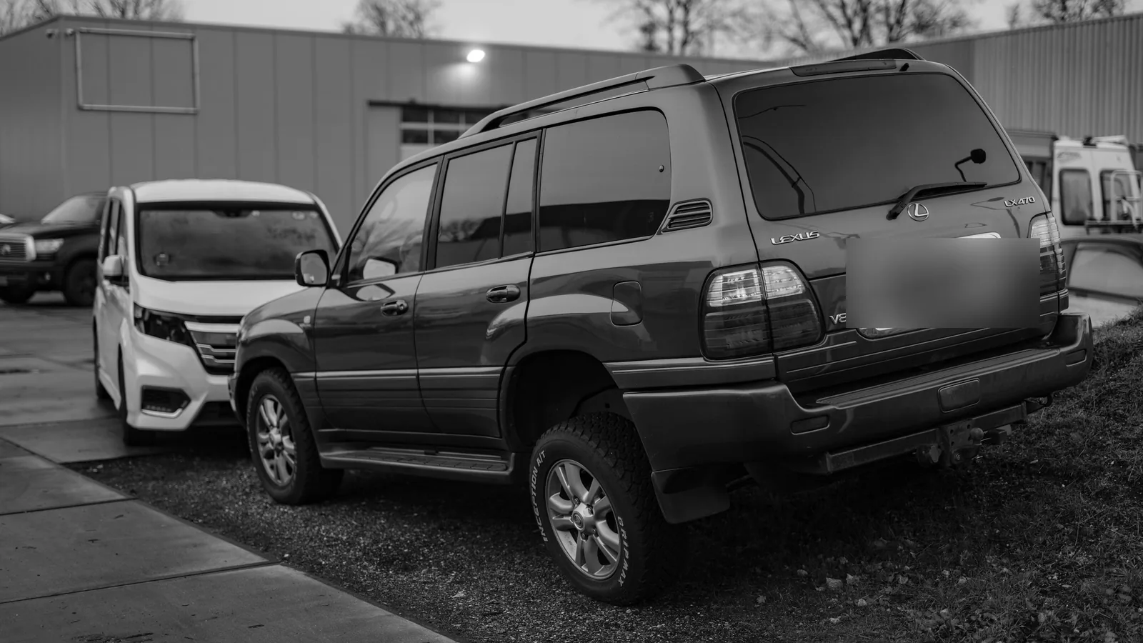 Photo en noir et blanc d’un grand SUV garé au bout d’un parking, contre un talus
