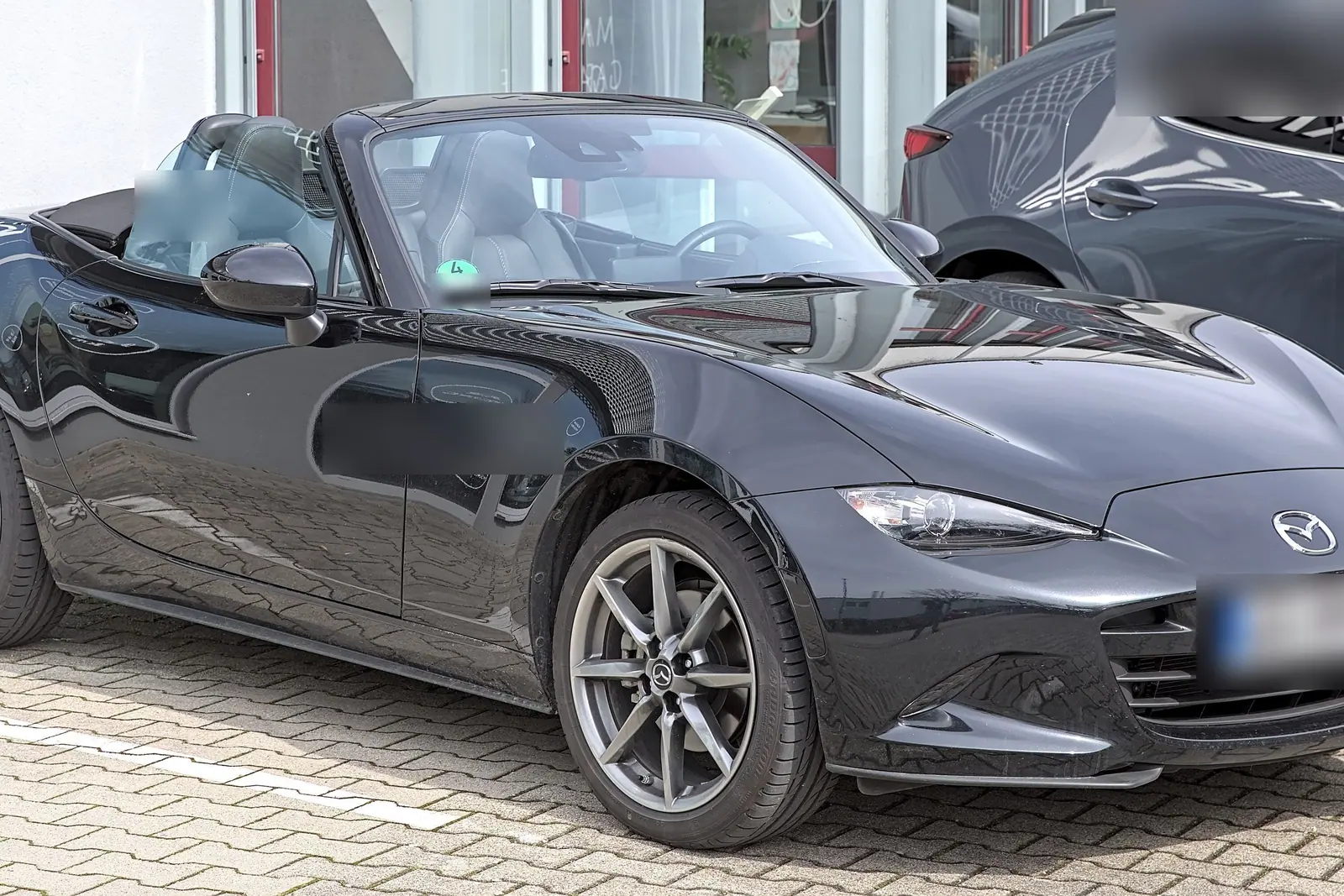 Mazda MX-5 noire décapotée garée devant un bâtiment
